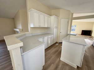 Kitchen with white cabinetry, wood finished floors, a peninsula, open floor plan, and a textured ceiling