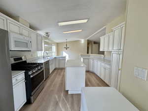 Kitchen featuring a peninsula, vaulted ceiling, appliances with stainless steel finishes, a chandelier, and white cabinetry