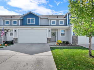 View of front of property with driveway, stone siding, an attached garage, a front lawn, and a shingled roof