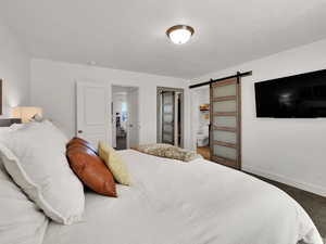 Primary Bedroom featuring a barn door, dark colored carpet, a textured ceiling, and connected bathroom