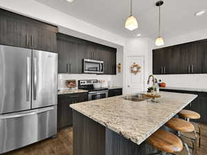 Kitchen with appliances with stainless steel finishes, decorative backsplash, pendant lighting, light stone countertops, and recessed lighting