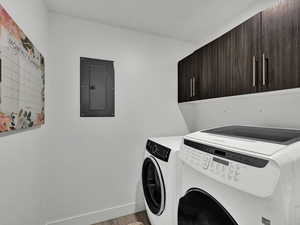 Laundry room featuring electric panel, cabinet space, washing machine and clothes dryer, and light wood-type flooring