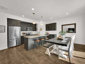 Kitchen with appliances with stainless steel finishes, a kitchen bar, dark brown cabinetry, pendant lighting, and decorative backsplash