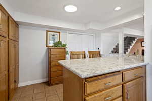Kitchen featuring light tile patterned flooring, brown cabinets, light stone counters, recessed lighting, and a breakfast bar