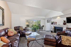Living area with lofted ceiling, carpet flooring, a fireplace with flush hearth, and a textured ceiling
