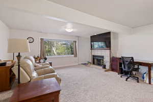Carpeted living room with a tiled fireplace and an office area