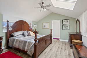 Bedroom with light wood-style floors, a ceiling fan, vaulted ceiling, and a skylight