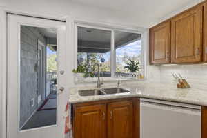Kitchen with brown cabinets, white dishwasher, plenty of natural light, and light stone counters