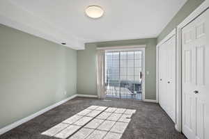 Unfurnished bedroom featuring dark colored carpet, multiple closets, and access to exterior