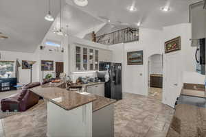 Kitchen with high vaulted ceiling, dark stone counters, a peninsula, arched walkways, and black appliances