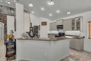 Kitchen with a breakfast bar, gray cabinets, dark stone counters, pendant lighting, and black range oven
