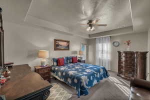 Bedroom featuring a raised ceiling, carpet flooring, a textured ceiling, and ceiling fan