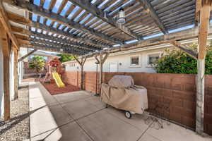 Fenced backyard with a playground, a patio area, and a pergola