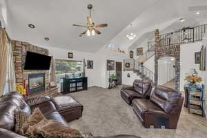 Carpeted living room with a fireplace, high vaulted ceiling, ceiling fan, stairway, and arched walkways