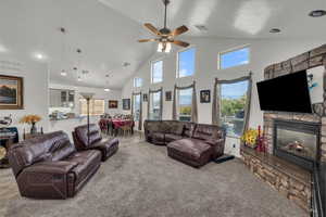 Carpeted living room featuring high vaulted ceiling, a stone fireplace, healthy amount of natural light, a ceiling fan, and recessed lighting