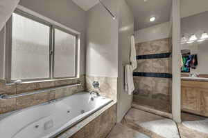 Bathroom featuring walk in shower, a jetted tub, vanity, and a walk in closet