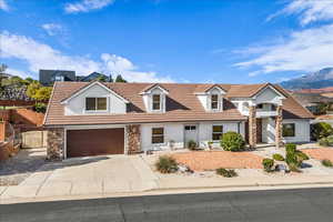 View of front of home with stucco siding, driveway, stone siding, a gate, and a garage