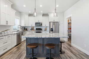 Kitchen featuring light stone counters, white cabinets, a kitchen bar, stainless steel appliances, and recessed lighting
