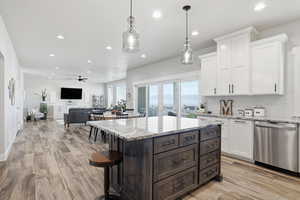 Kitchen featuring white cabinets, dark brown cabinets, light stone counters, stainless steel dishwasher, and hanging light fixtures