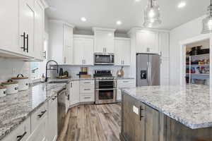 Kitchen featuring recessed lighting, appliances with stainless steel finishes, white cabinets, light stone countertops, and light wood-style flooring