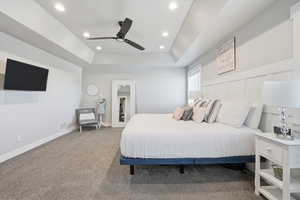 Carpeted bedroom featuring a raised ceiling, recessed lighting, and a ceiling fan