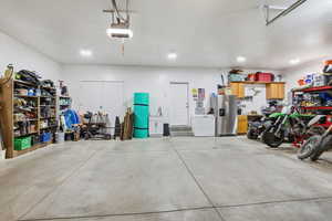 Garage featuring stainless steel refrigerator with ice dispenser, white fridge, and a garage door opener
