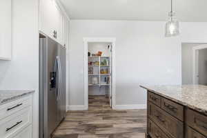 Kitchen featuring stainless steel refrigerator with ice dispenser, light stone counters, decorative light fixtures, white cabinetry, and dark wood-style floors