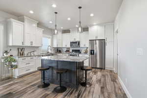 Kitchen with appliances with stainless steel finishes, a kitchen bar, light stone counters, white cabinetry, and recessed lighting