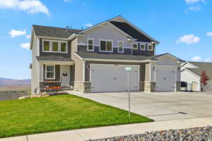 Craftsman house with stone siding, concrete driveway, board and batten siding, and a front yard