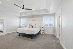 Carpeted bedroom featuring a raised ceiling, multiple windows, a ceiling fan, and recessed lighting