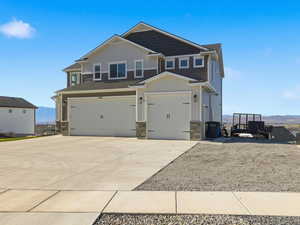 Craftsman-style home with board and batten siding, stone siding, a garage, concrete driveway, and a mountain view
