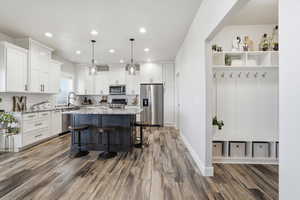 Kitchen featuring stainless steel appliances, white cabinetry, decorative light fixtures, a breakfast bar, and recessed lighting