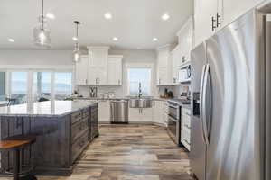 Kitchen with stainless steel appliances, a kitchen bar, white cabinetry, light stone counters, and dark brown cabinets