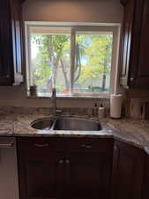 Kitchen with dark brown cabinets, light stone countertops, and stainless steel dishwasher