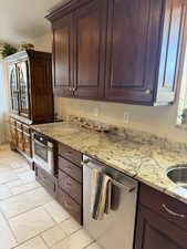 Kitchen with stainless steel dishwasher, light stone countertops, dark brown cabinets, and stone tile floors