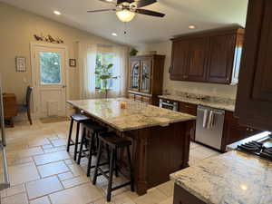 Kitchen with recessed lighting, light stone counters, stainless steel appliances, dark brown cabinets, and a kitchen island