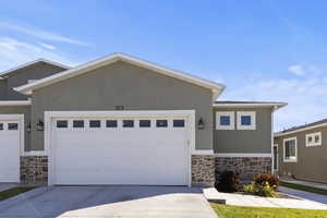 View of front facade with stone siding, stucco siding, concrete driveway, and an attached garage