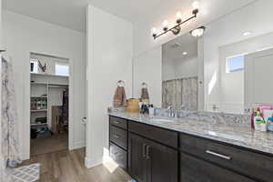Full bath featuring vanity, light wood-style floors, curtained shower, and a walk in closet