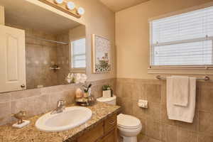 Full bath featuring vanity, a shower, tile patterned flooring, a wainscoted wall, and tile walls