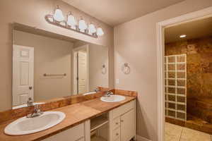 Full bath featuring a walk in shower, double vanity, and light tile patterned floors