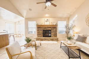Living room featuring a ceiling fan, a stone fireplace, plenty of natural light, and light tile patterned flooring