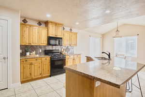 Kitchen featuring black appliances, light stone counters, hanging light fixtures, decorative backsplash, and a kitchen island with sink