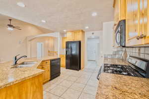 Kitchen with arched walkways, black appliances, light stone counters, recessed lighting, and a textured ceiling