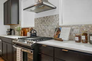Kitchen with stainless steel range with gas cooktop, island exhaust hood, backsplash, dark cabinets, and light stone counters
