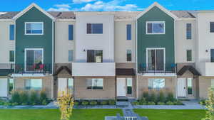 View of front of property with a balcony, a front yard, and brick siding