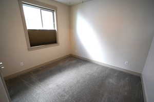 Spare room featuring dark colored carpet and baseboards