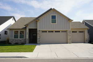 Craftsman-style home featuring roof with shingles, stone siding, board and batten siding, driveway, and a front yard