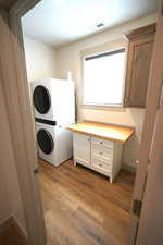 Laundry room with dark wood-style floors, stacked washer / dryer, and cabinet space