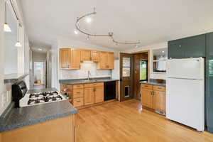Kitchen with white appliances, dark countertops, vaulted ceiling, light wood-type flooring, and decorative light fixtures