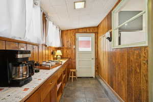 Kitchen featuring light countertops, wooden walls, brown cabinetry, and dark stone finish floors